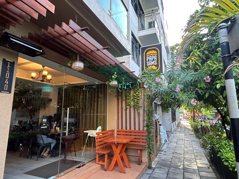 Timber-pergola terrace at Papa Sam's with a wooden bench, glass frontage and the burger logo sign