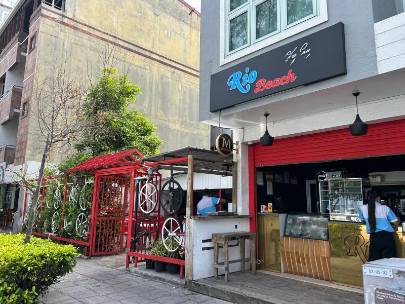 Rio Beach open-front cafe with red awning, food counter and bicycle wheels mounted on a red fence outside