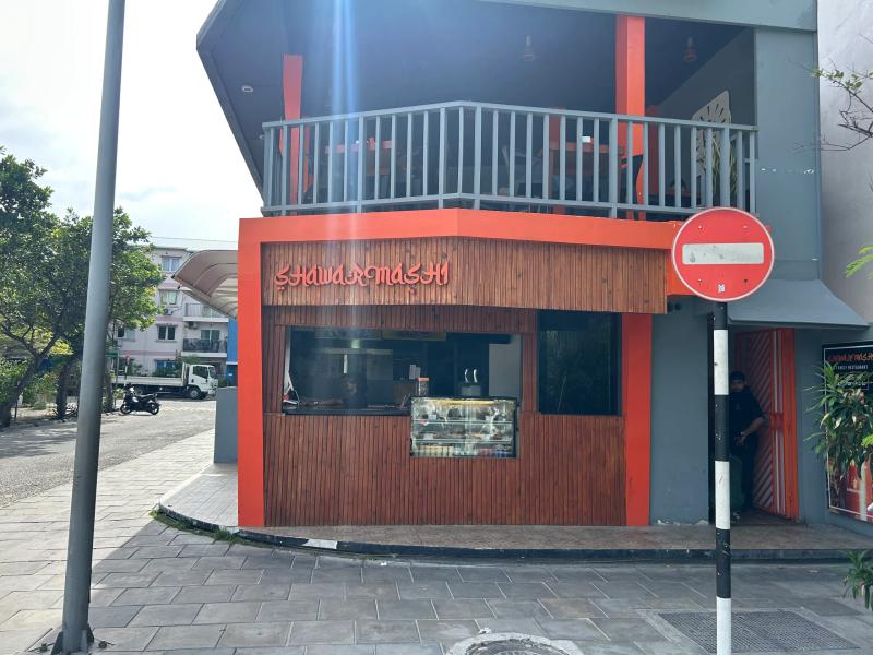 Shawarmashi orange timber corner kiosk with counter and food display, beside a no-entry sign and balcony seating