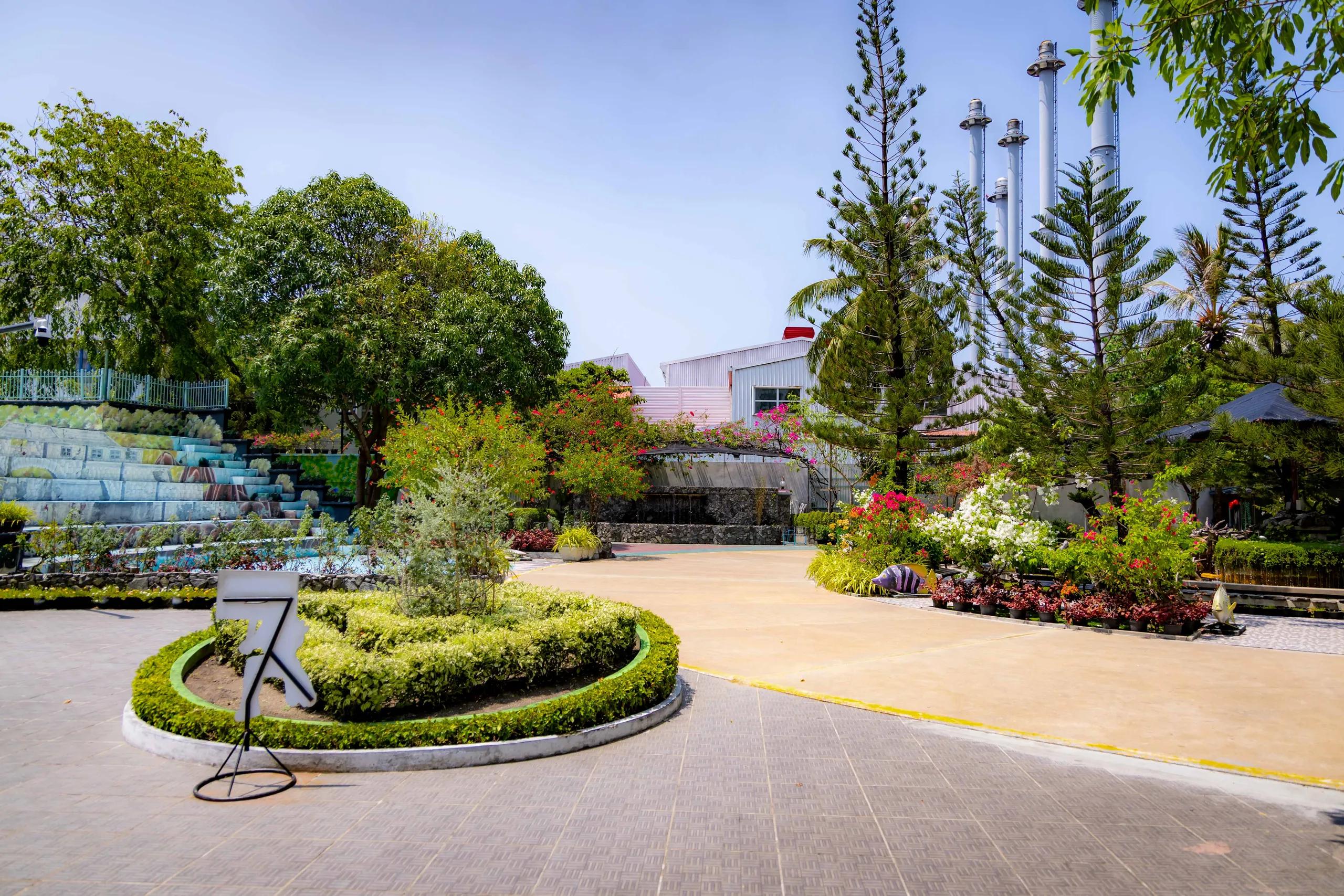 Landscaped garden with flowering shrubs, a paved courtyard and tall pines at Kudakudhinge Bageecha children's park