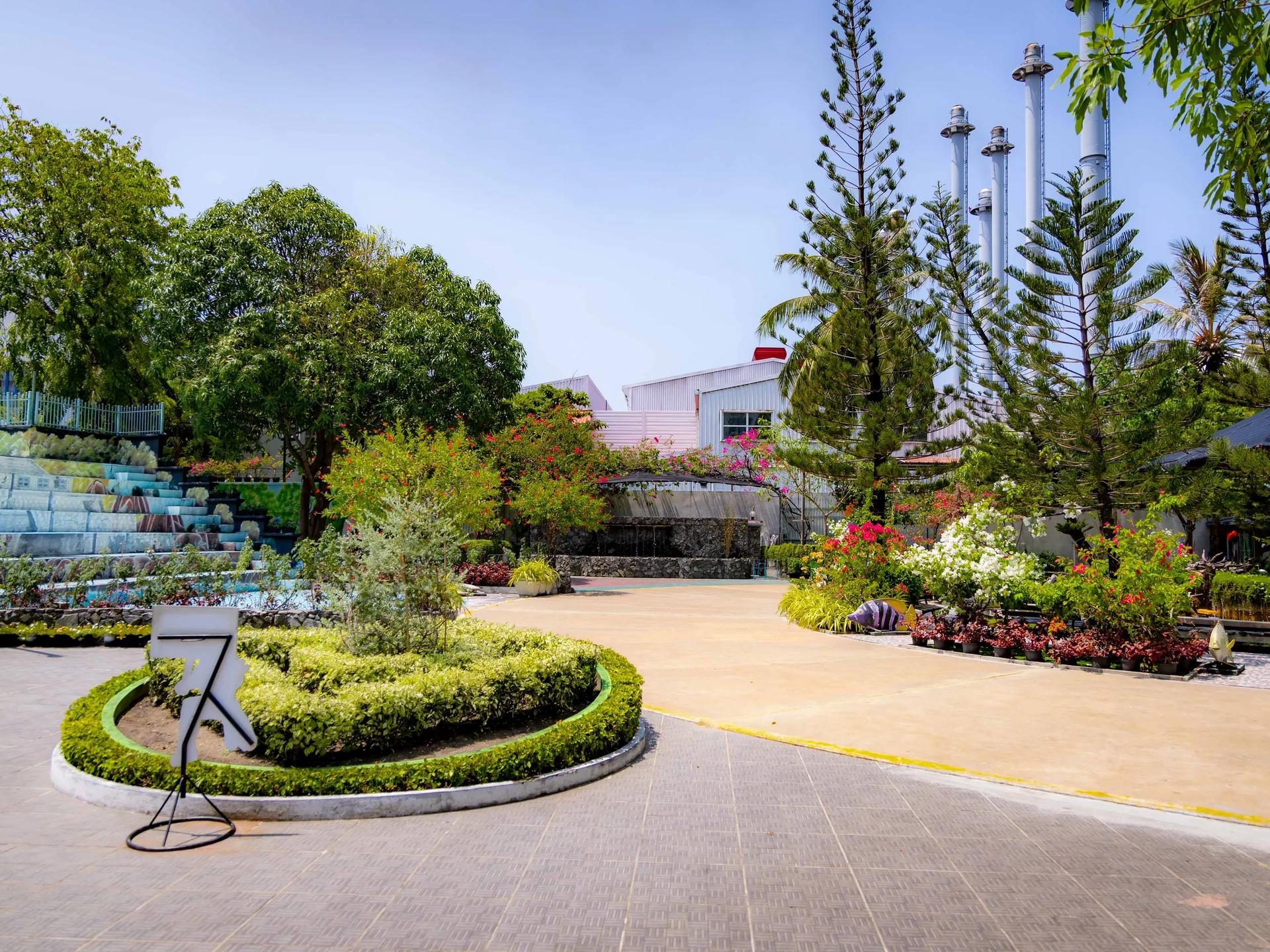 Landscaped garden with flowering shrubs, a paved courtyard and tall pines at Kudakudhinge Bageecha children's park