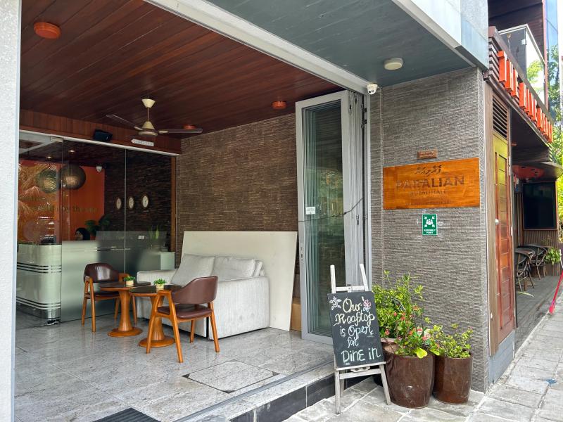 Open lounge entrance at Paralian with a sofa, wooden chairs and a chalkboard reading Our Rooftop is Open for Dine In