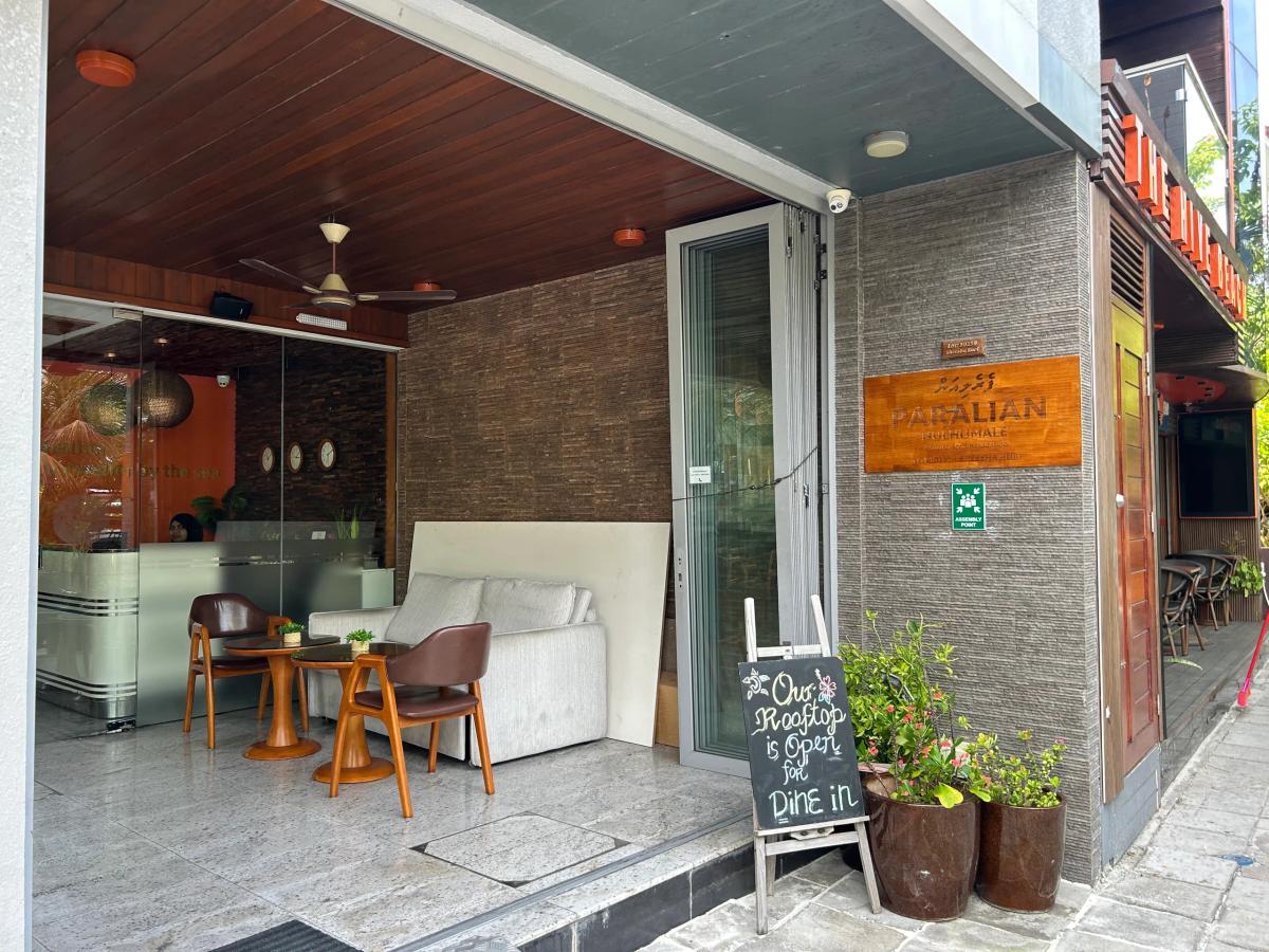 Open lounge entrance at Paralian with a sofa, wooden chairs and a chalkboard reading Our Rooftop is Open for Dine In