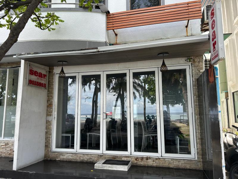 The Sear by Seera glass-fronted restaurant reflecting beach palms, with a red sign reading phone 9115913