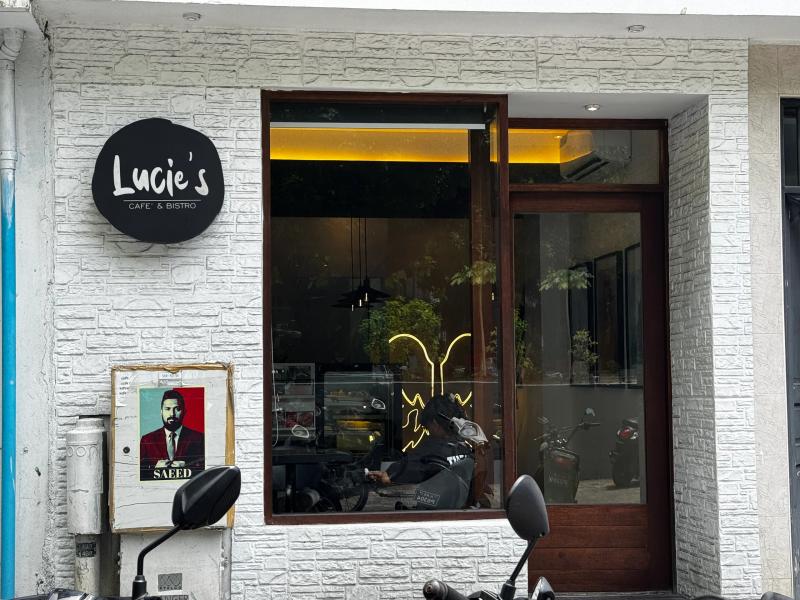 Round black Lucie's Cafe & Bistro sign on a white brick wall beside a large window into the dim cafe interior