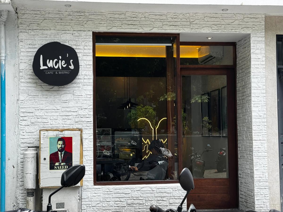 Round black Lucie's Cafe & Bistro sign on a white brick wall beside a large window into the dim cafe interior