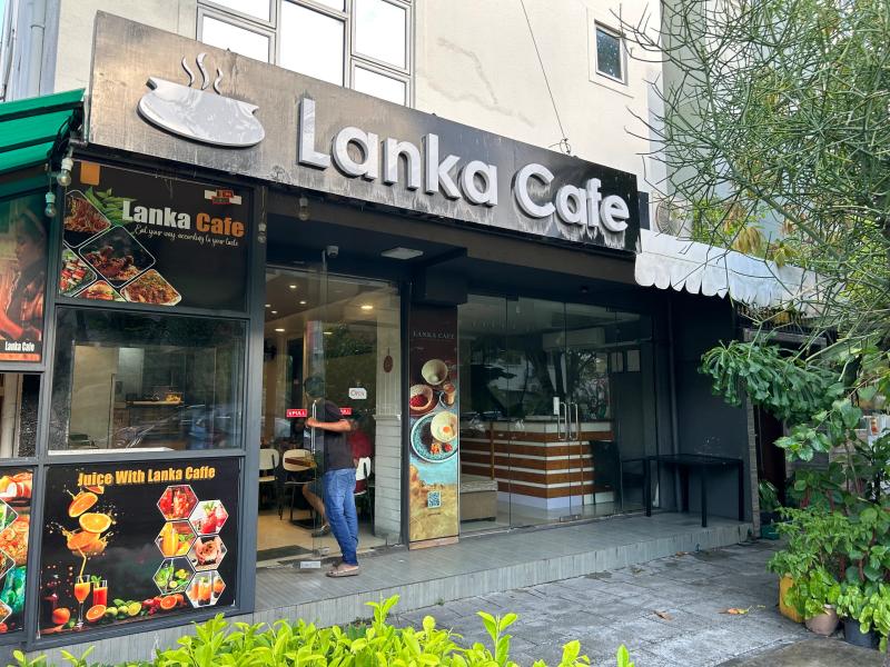 Lanka Cafe storefront with a black signboard, food photo posters in the windows and a person at the glass door