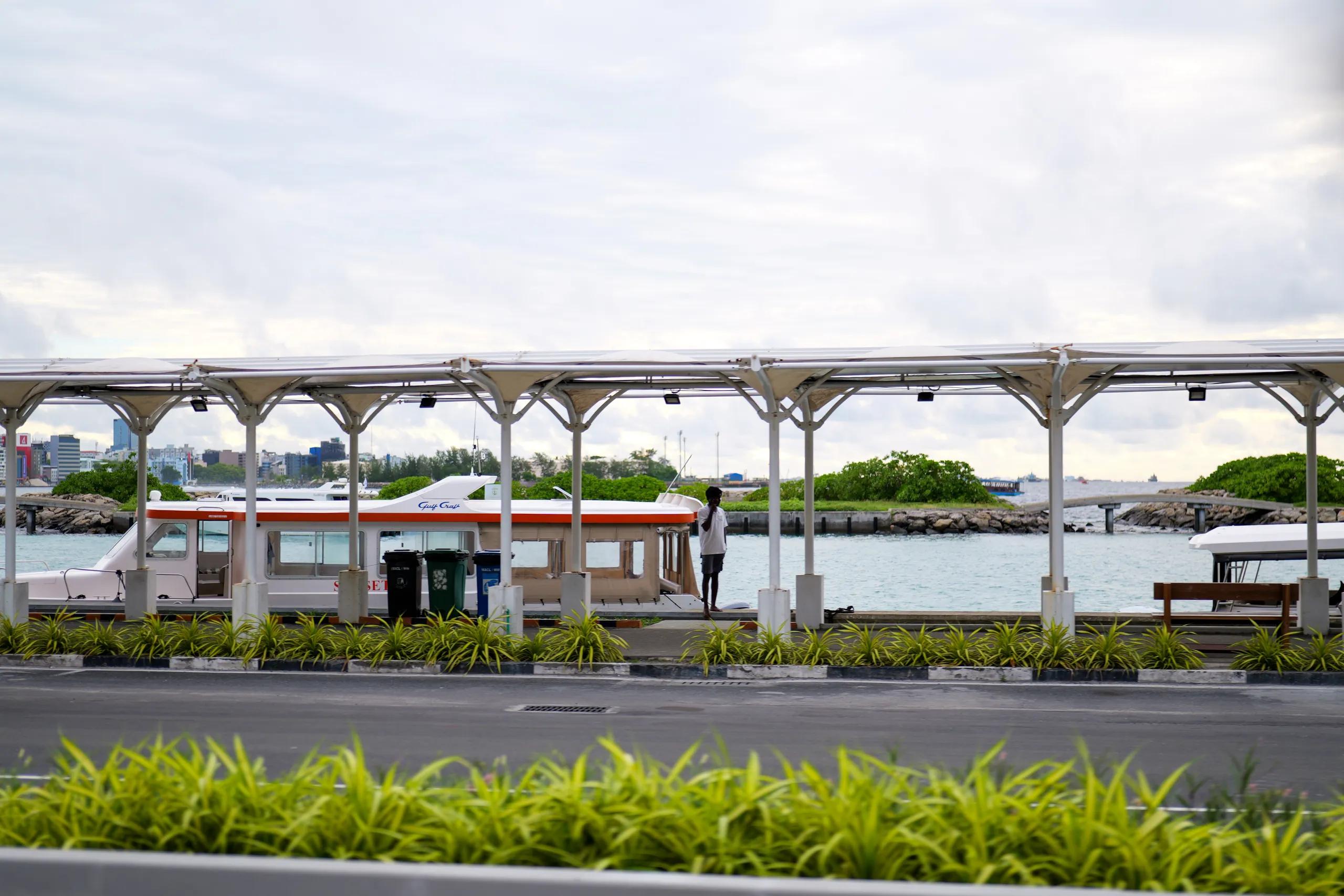 The covered jetty at Velana International Airport, with speedboats moored and Malé's skyline across the water