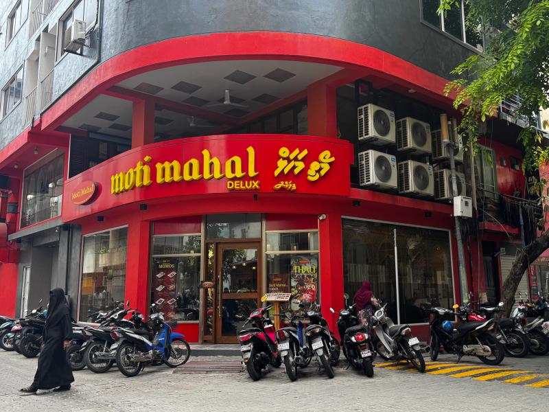 Red corner facade of Moti Mahal Delux restaurant with parked motorbikes and pedestrians on the street