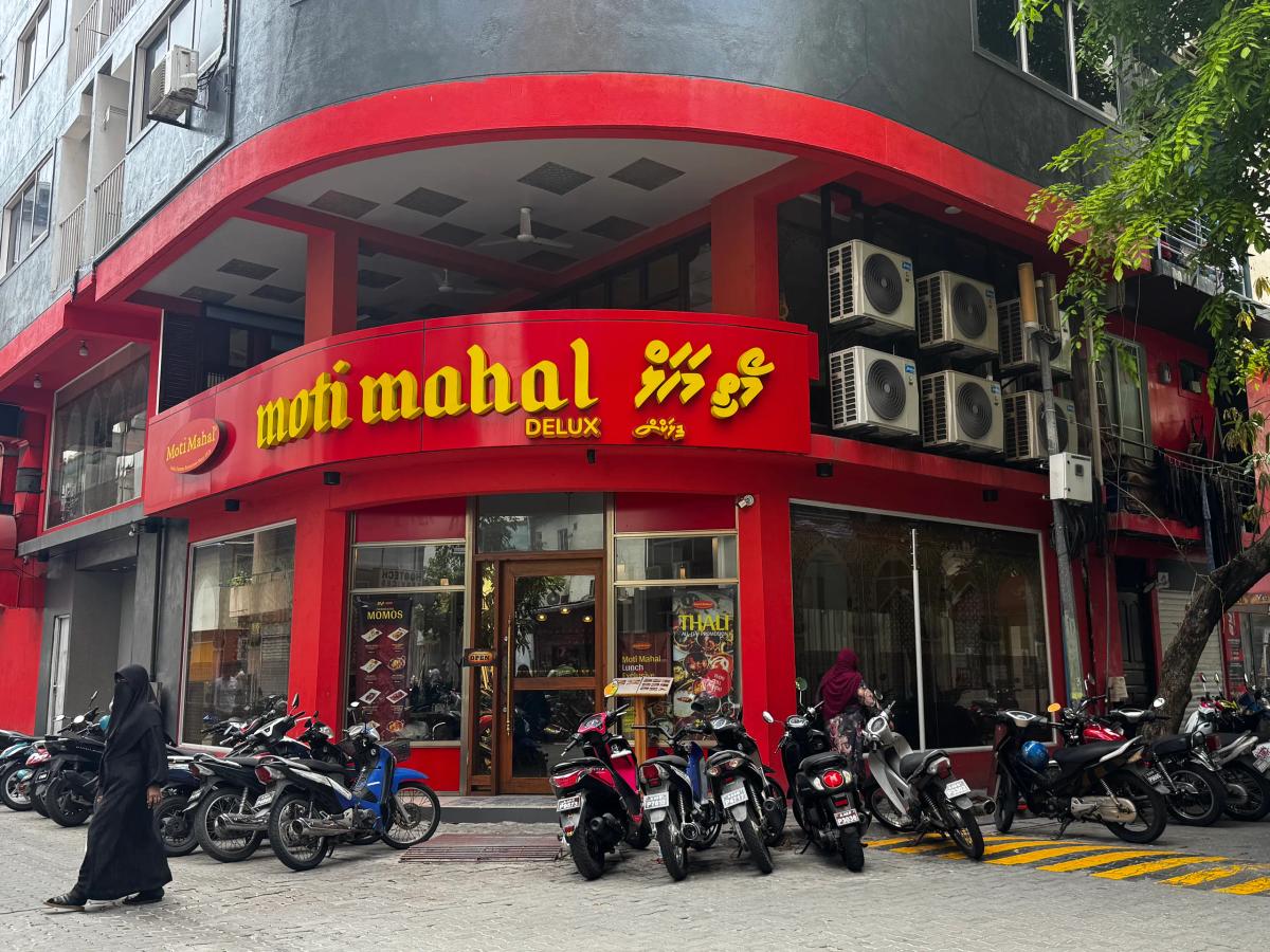 Red corner facade of Moti Mahal Delux restaurant with parked motorbikes and pedestrians on the street