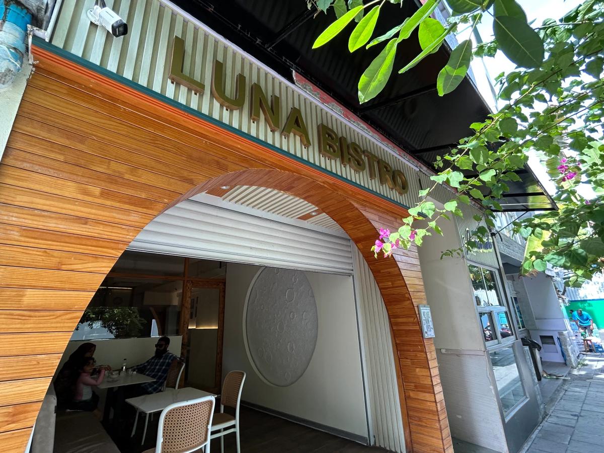 Wood-clad arched entrance of Luna Bistro with gold lettering, a moon-crater wall panel and diners seated inside