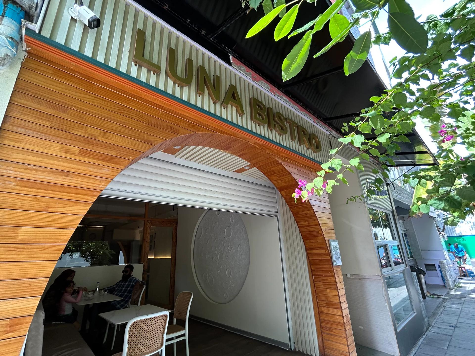 Wood-clad arched entrance of Luna Bistro with gold lettering, a moon-crater wall panel and diners seated inside