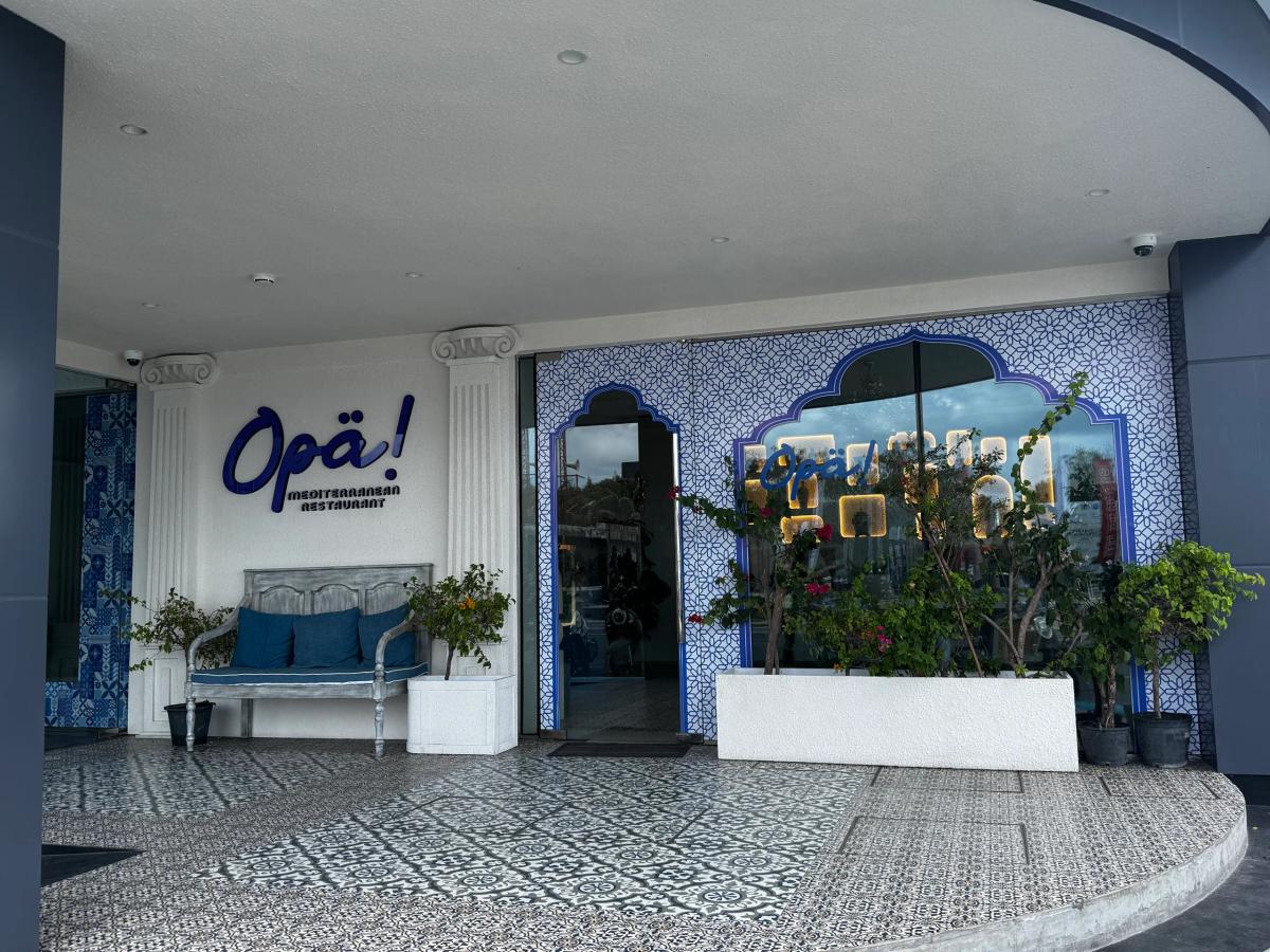 Blue-and-white Mediterranean facade of Opa! restaurant with patterned tiles, columns and a cushioned bench