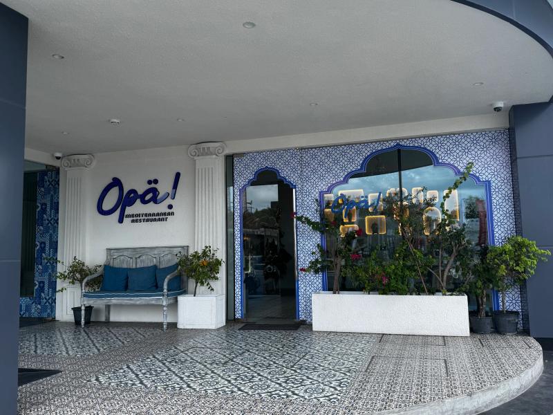 Blue-and-white Mediterranean facade of Opa! restaurant with patterned tiles, columns and a cushioned bench
