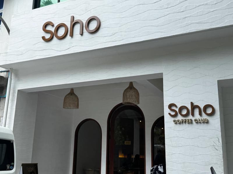 Soho Coffee Club white textured facade with brown lettering, arched entrances and woven pendant lamps