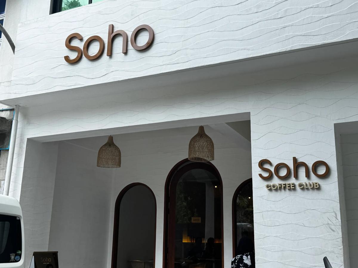 Soho Coffee Club white textured facade with brown lettering, arched entrances and woven pendant lamps