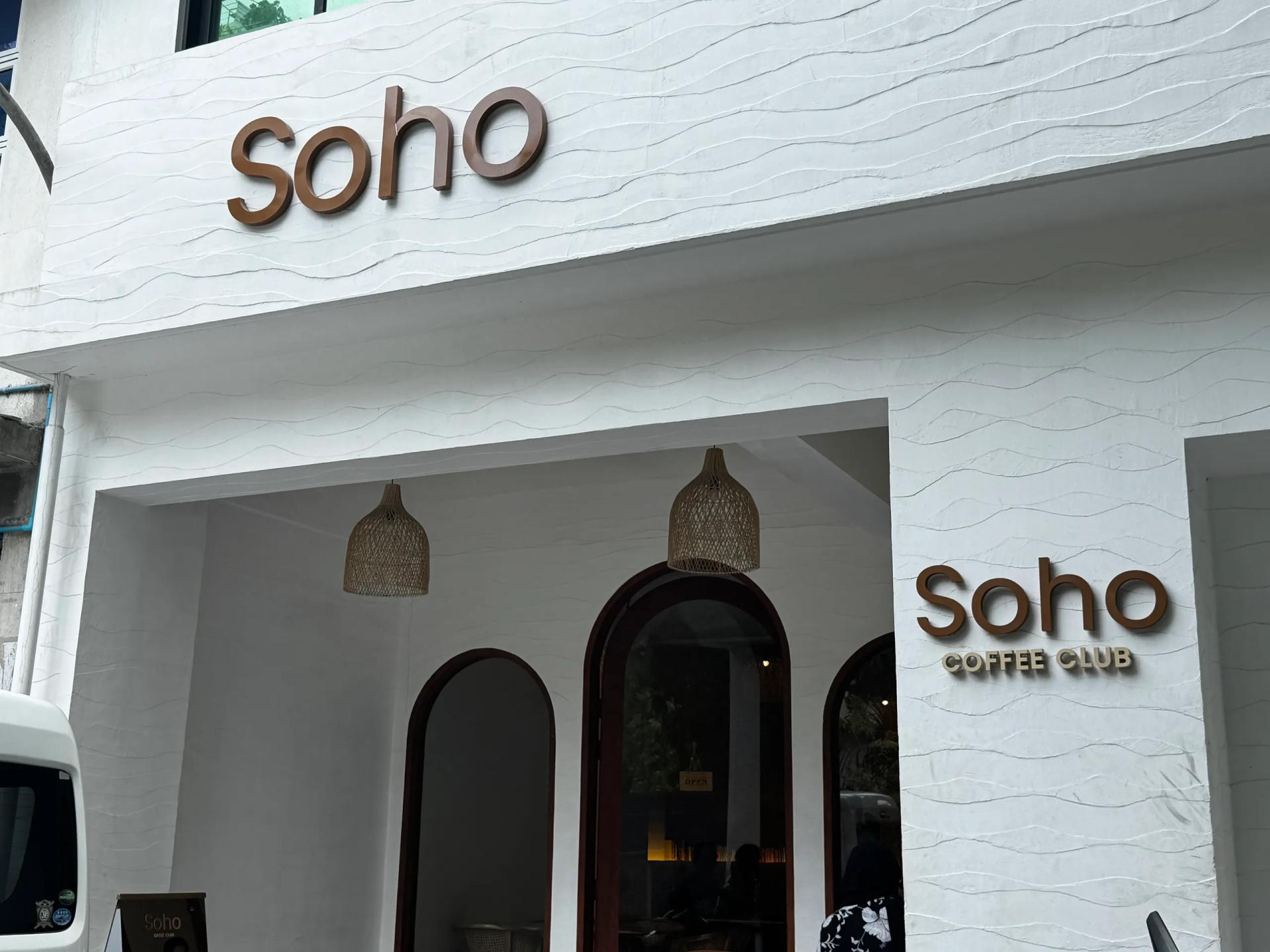Soho Coffee Club white textured facade with brown lettering, arched entrances and woven pendant lamps