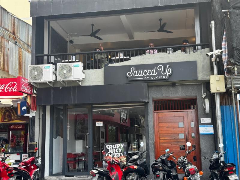 Sauced Up by Lucies two-storey shopfront with balcony seating, a Crispy Juicy Cheesy banner and parked motorbikes