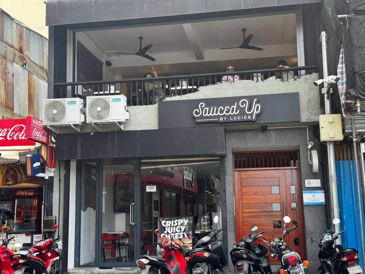 Sauced Up by Lucies two-storey shopfront with balcony seating, a Crispy Juicy Cheesy banner and parked motorbikes