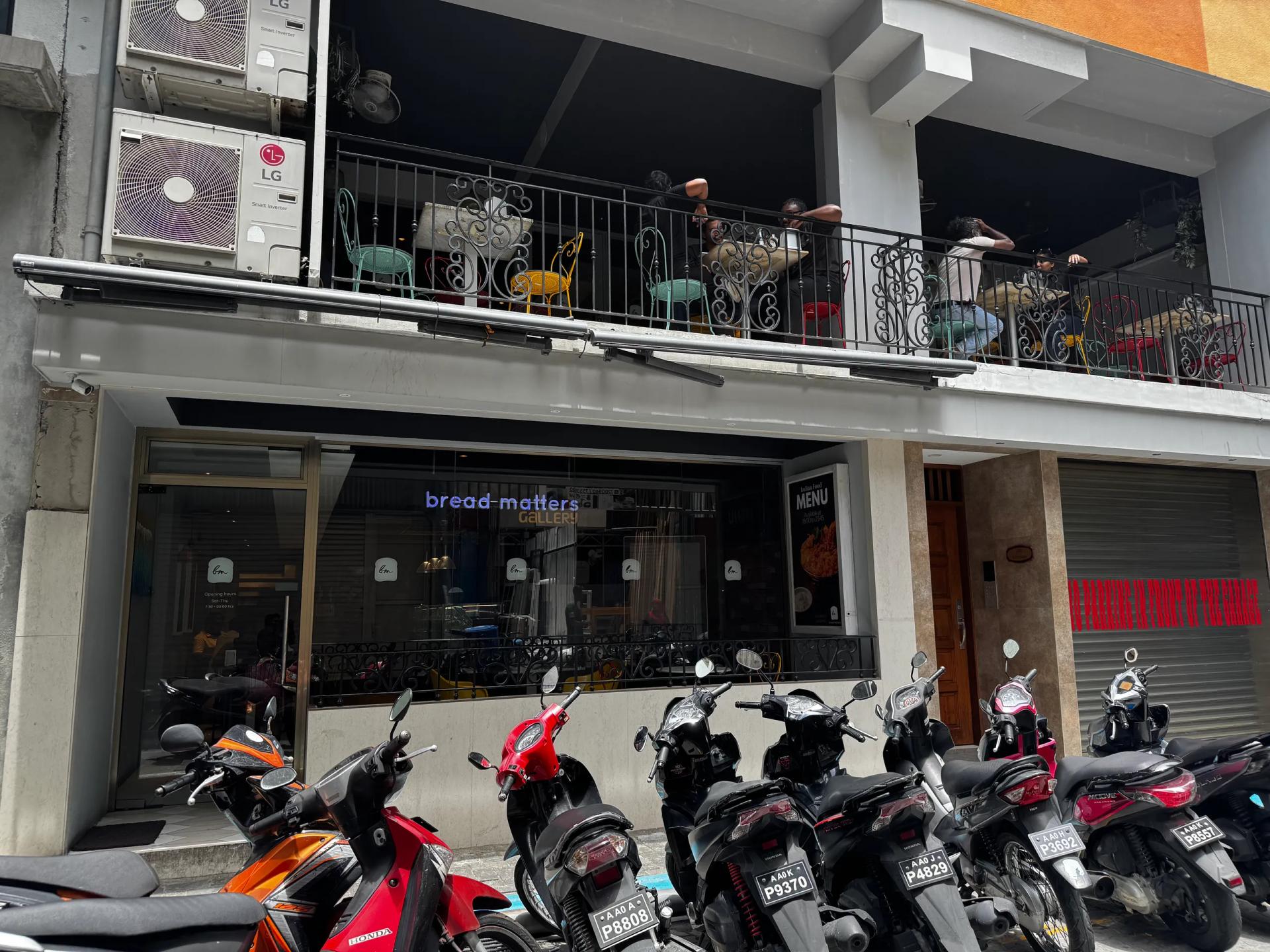 bread matters Gallery with a balcony of colourful bistro chairs above and motorbikes parked out front