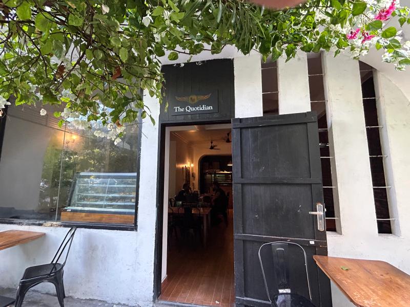 Open black doorway signed The Quotidian, with a pastry display case and diners visible inside under flowering vines