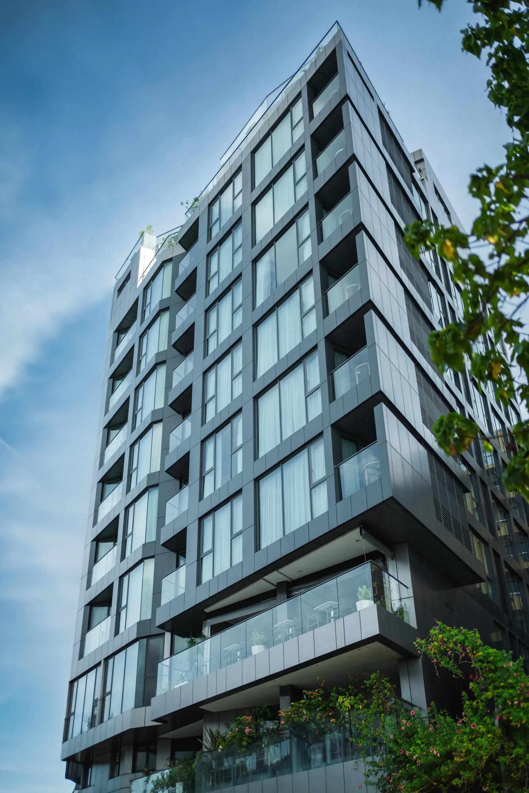 Glass and grey panelled facade of Maagiri Hotel rising over street greenery in Malé