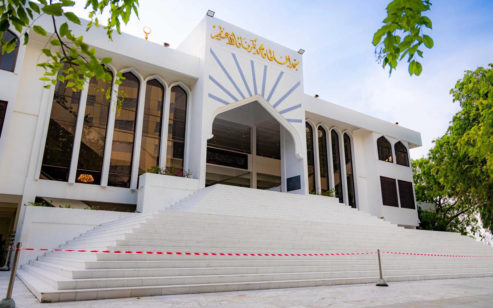 Broad white steps leading up to the arched entrance of the Islamic Centre, with gold Arabic script on the facade