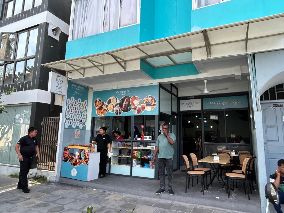 Teal Keyla Beach Cafe storefront with a food display counter and outdoor tables, staff and customers nearby