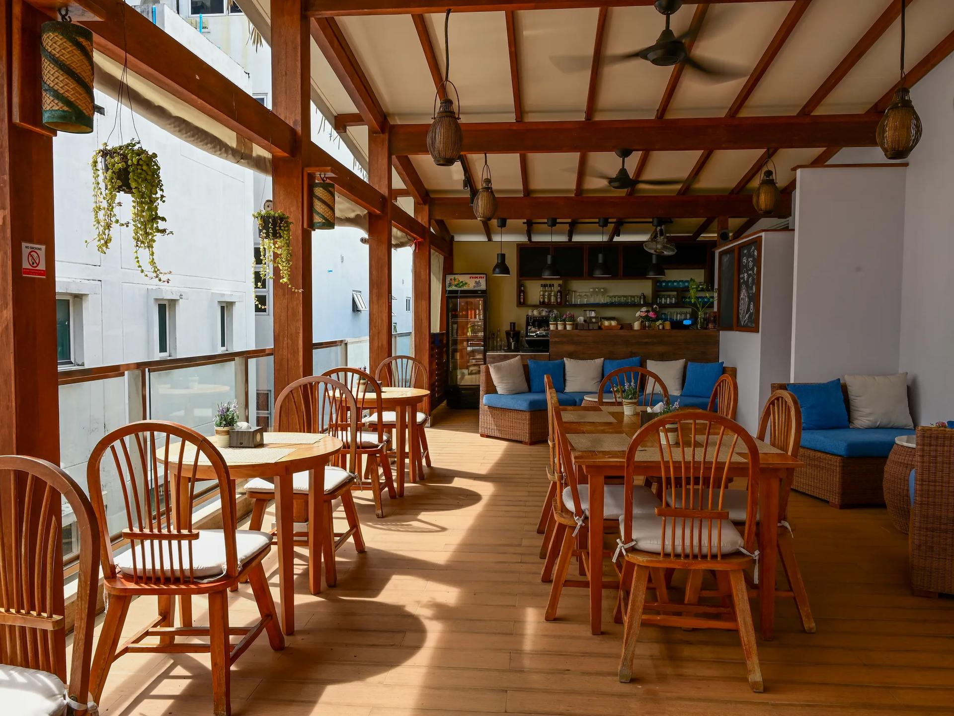 High Tide Restaurant's open-air timber dining terrace at Seasalter Maldives, with round wooden tables, blue lounge seating and a bar at the back