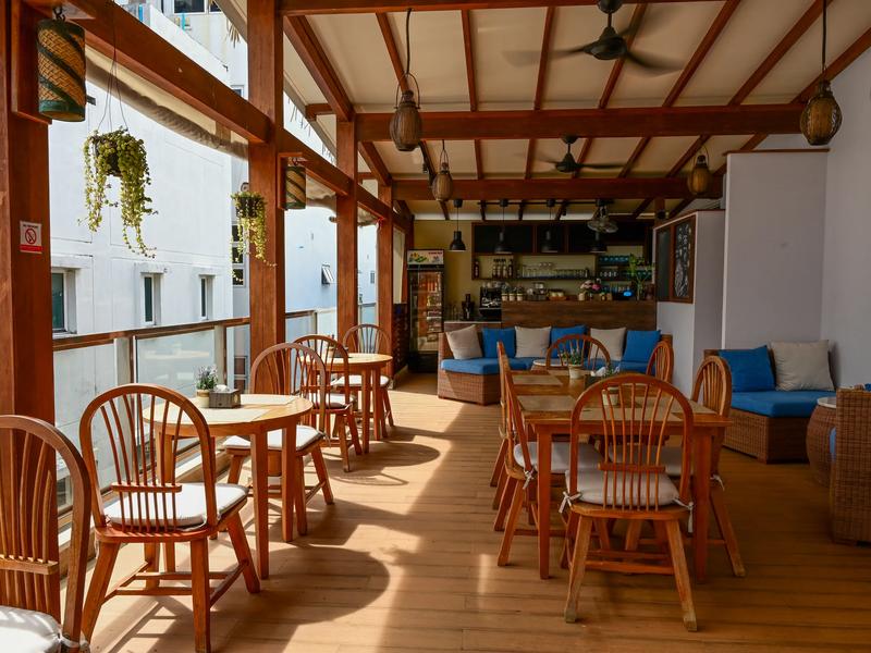 High Tide Restaurant's open-air timber dining terrace at Seasalter Maldives, with round wooden tables, blue lounge seating and a bar at the back
