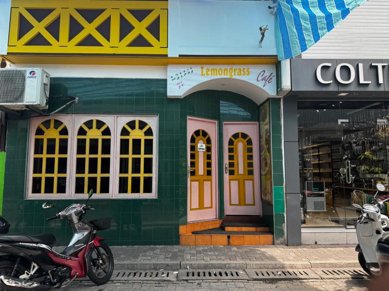 Green-tiled facade of Lemongrass Cafe with arched yellow windows, pink doors and a motorbike parked outside