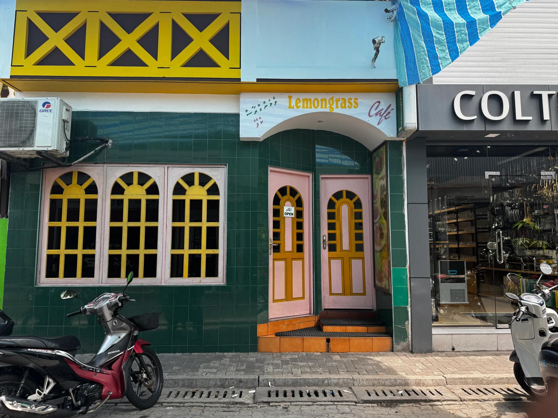 Green-tiled facade of Lemongrass Cafe with arched yellow windows, pink doors and a motorbike parked outside