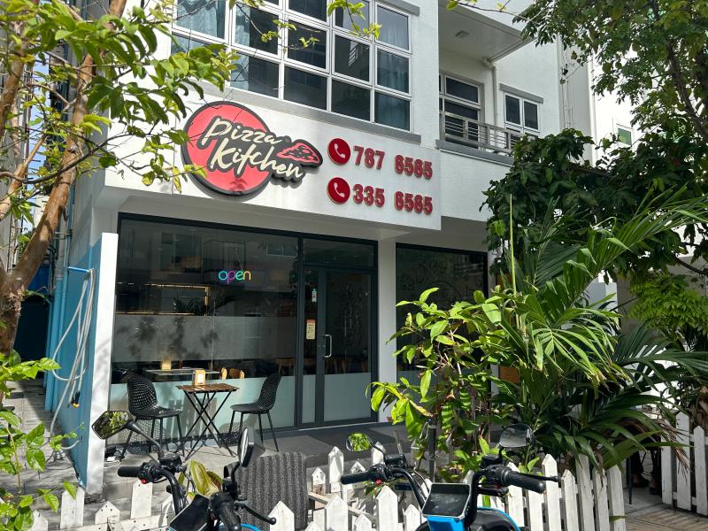 Pizza Kitchen storefront with a red logo sign, glass front and outdoor table behind a white picket fence