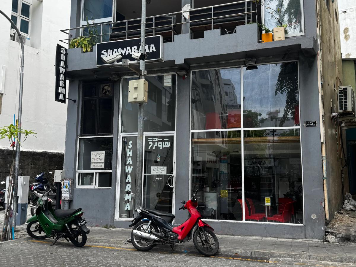 Shawarma restaurant grey shopfront with black vertical signs, glass front and motorbikes parked on the street
