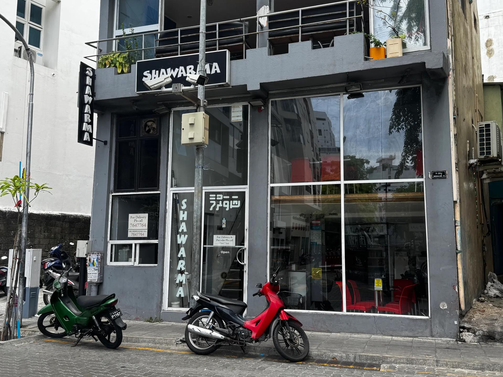 Shawarma restaurant grey shopfront with black vertical signs, glass front and motorbikes parked on the street