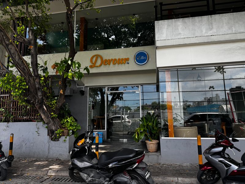 Devour by Ellies' script sign above a glass-walled front, shaded by a large tree