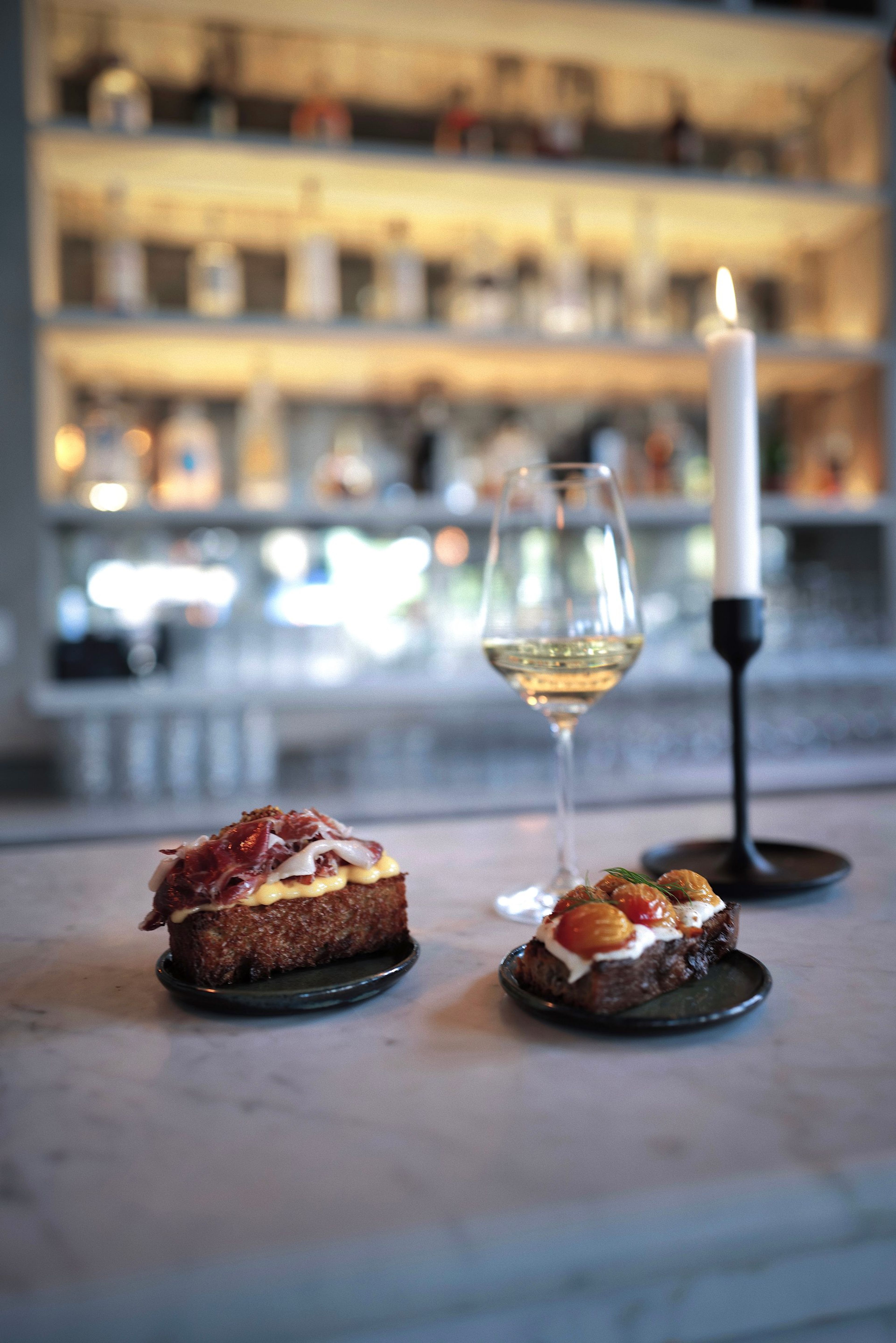 Iberico toast and tomato toast on the marble bar, with a glass of white wine and a candle