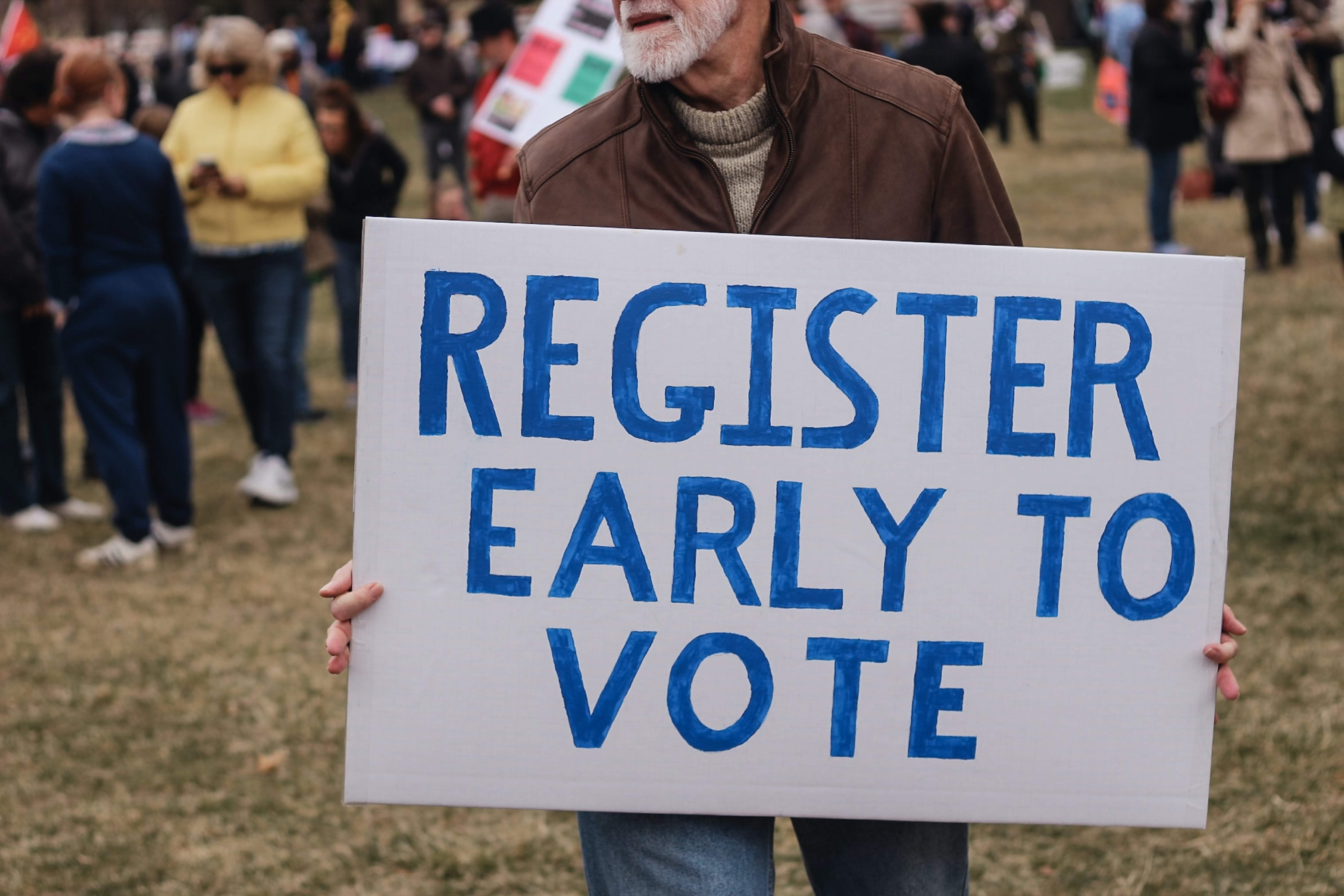 Man holding up a hand painted sign that reads, "register early to vote"