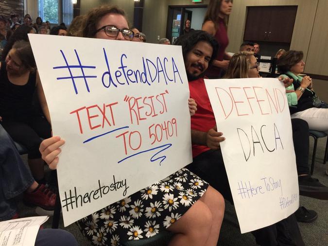 Two people holding up signs to text resist to 50409 to defend DACA