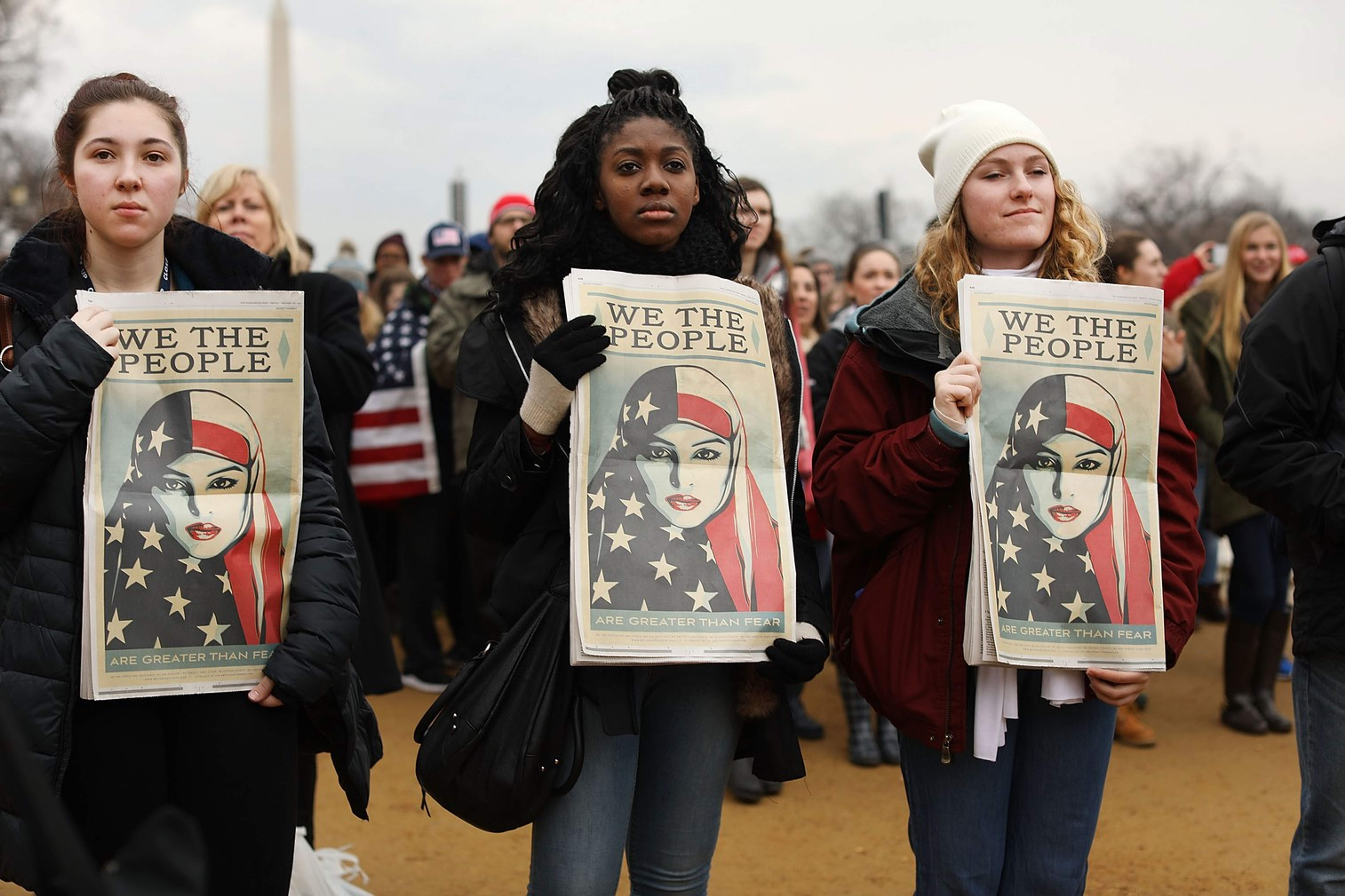 Three women holding up "we the people" posters