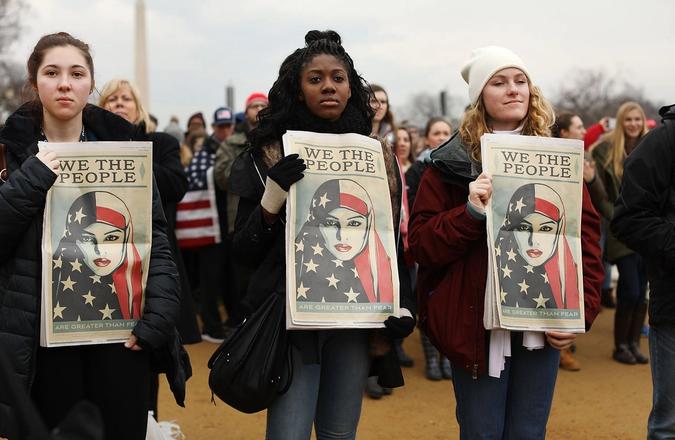 Three women holding up "we the people" posters