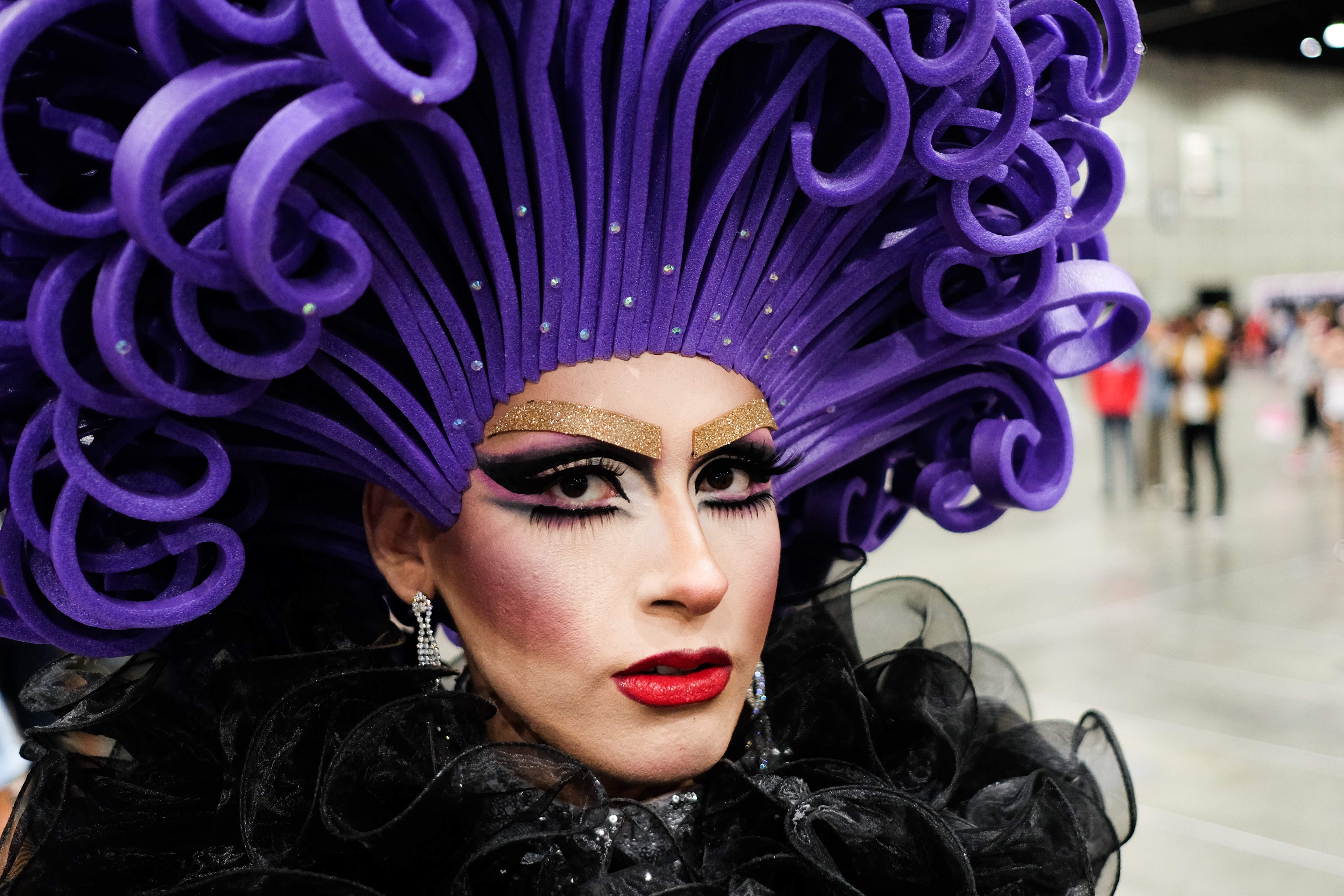 Photo of a drag queen with bright purple hair, red lipstick, and stage makeup.