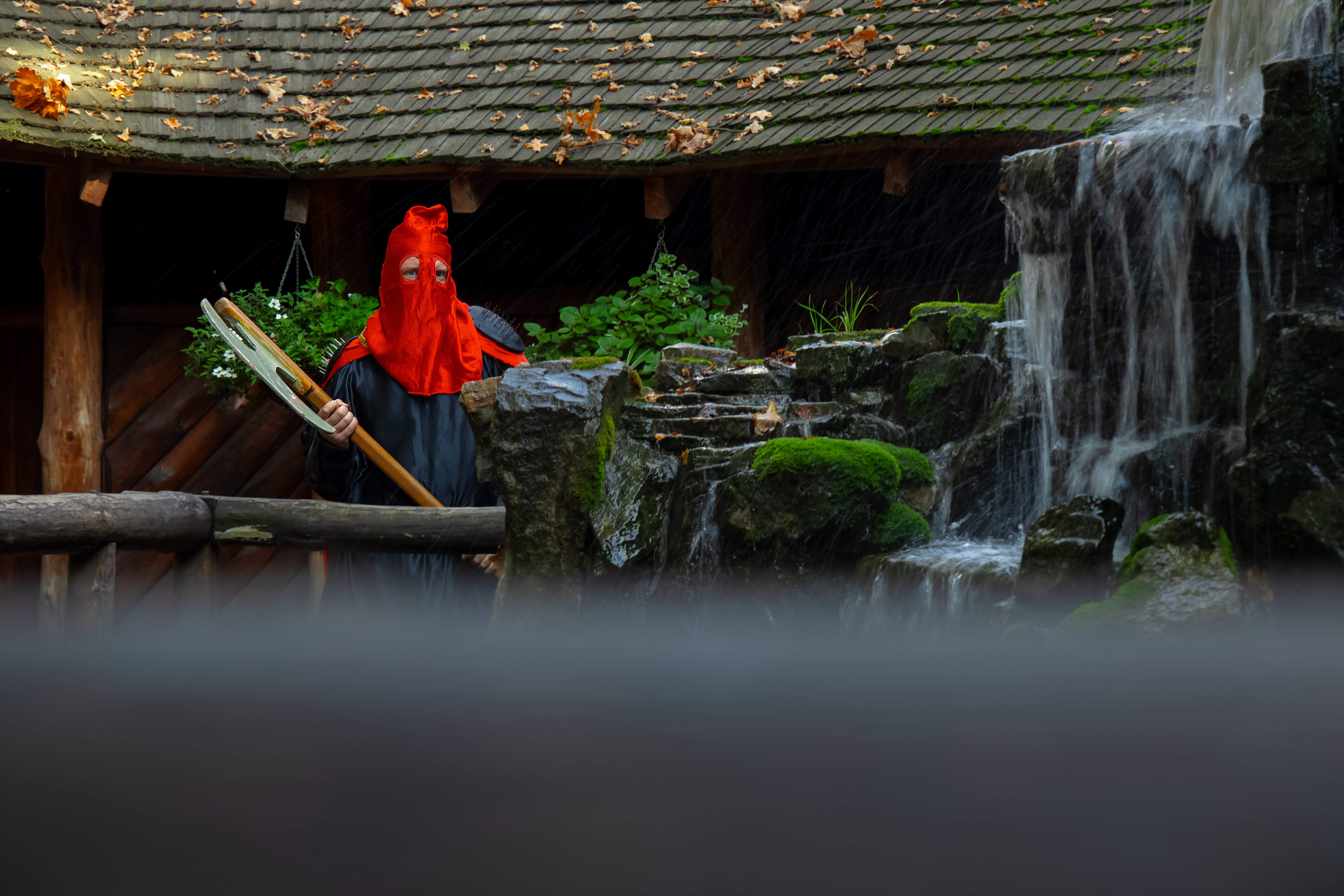 Executioner role play cosplay by adult person in costume and ax, foreground noise from fountain drops