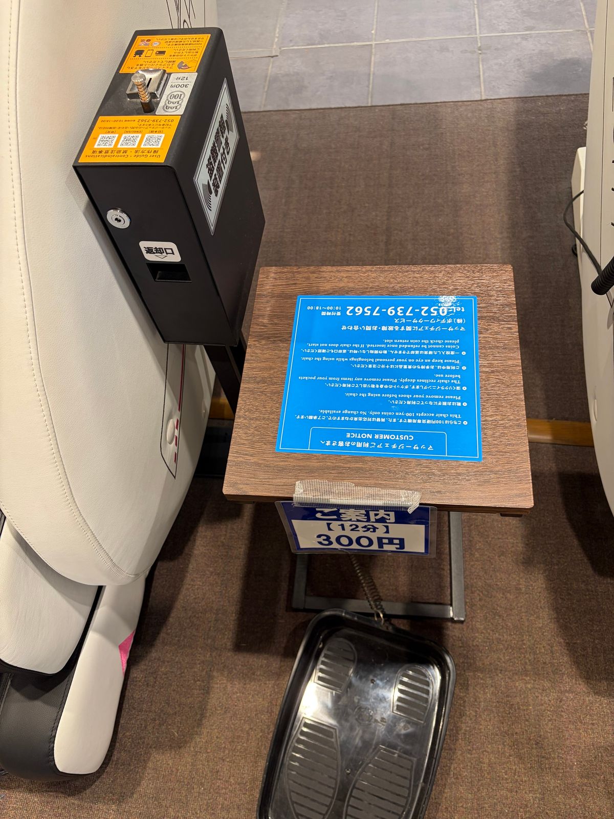 マッサージチェア横のコイン投入機と案内板。「ご案内【12分】300円」と書かれている