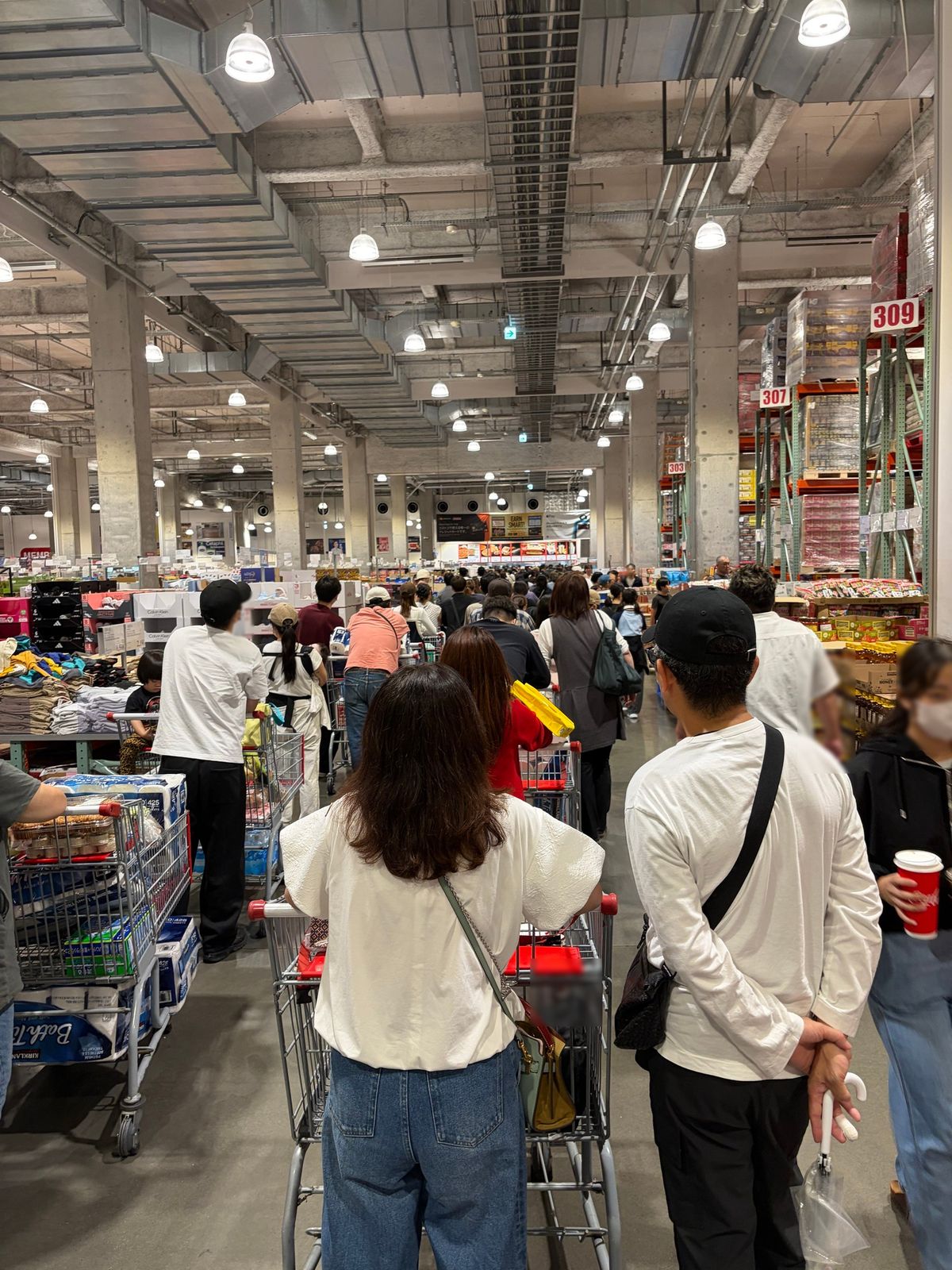 コストコの店内。カートを押した買い物客の列が、通路の奥まで続いている