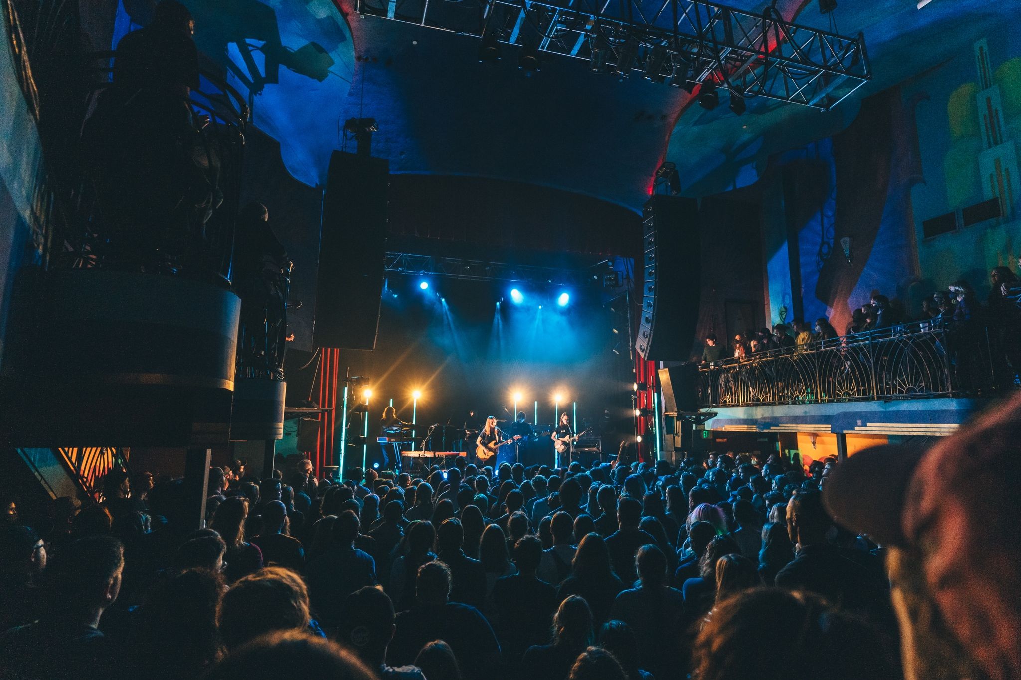 Crowd on the floor facing a lit stage, balcony on the right