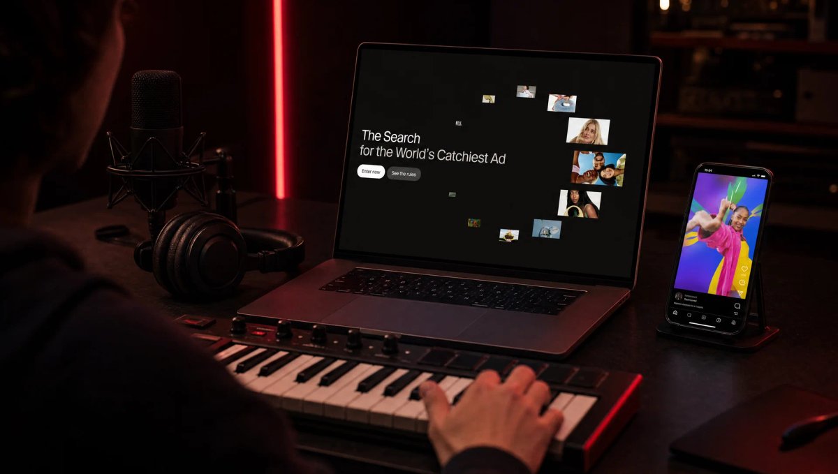 حاسوب محمول يعرض صفحة مسابقة The Search for the World’s Catchiest Ad من ElevenLabs، أمام لوحة مفاتيح MIDI وميكروفون استوديو وسماعات وهاتف يعرض إعلانًا عموديًا ملوّنًا، في استوديو مظلم بإضاءة حمراء