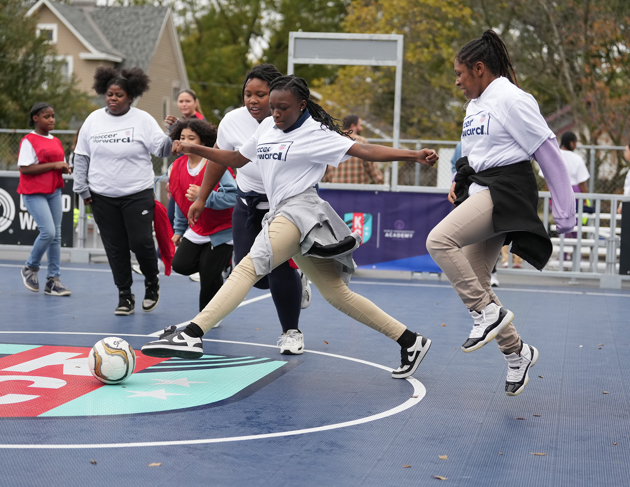 Girls play a small-sided soccer game at school, competing for the ball on a hard court during a Soccer Forward activity.