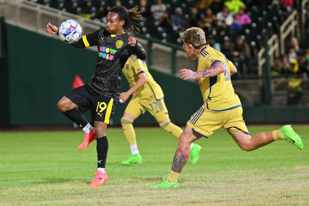 Zico Bailey with the ball as two opponents close in during a match