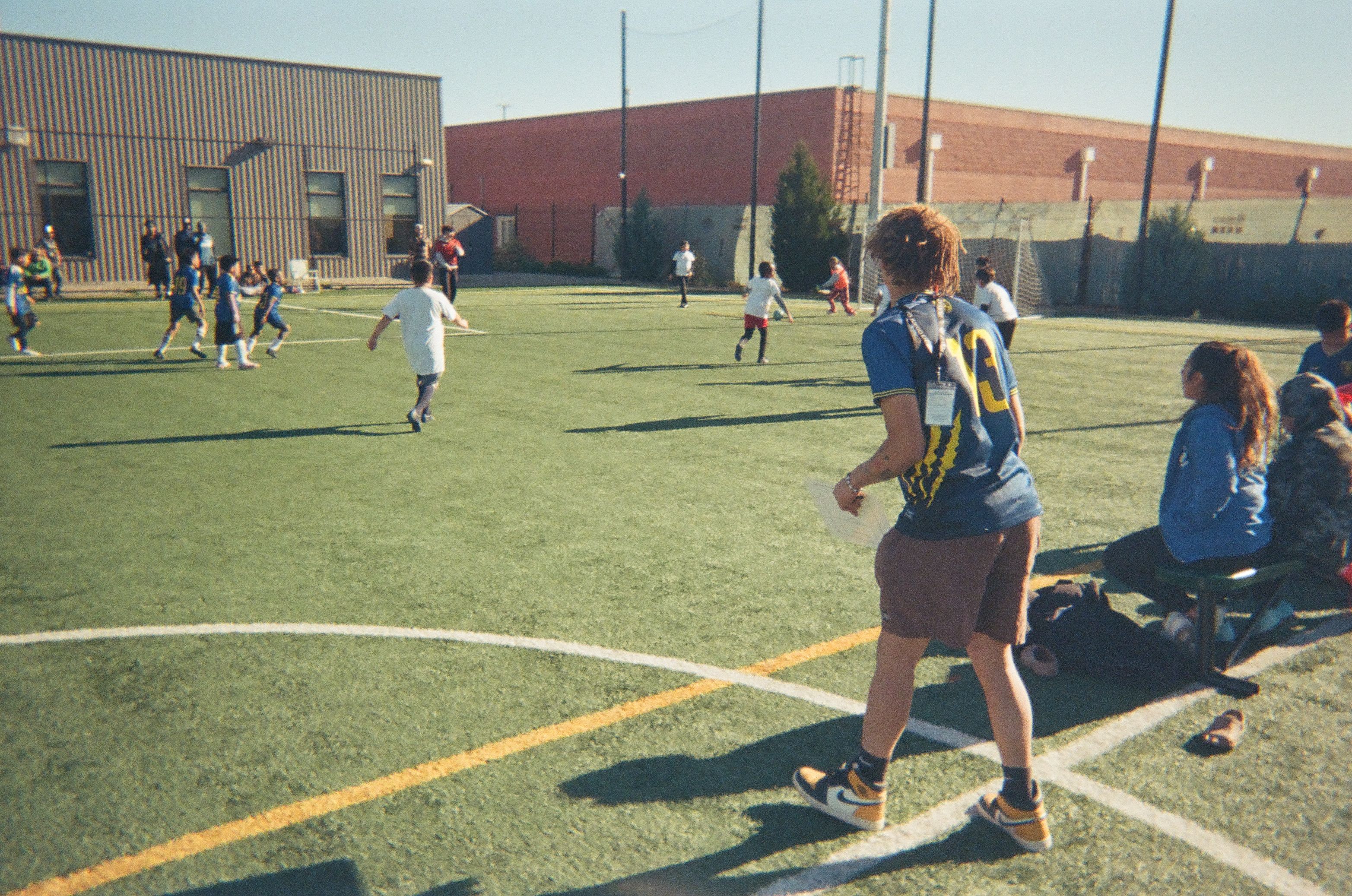 Coach watching from the sideline during a youth soccer match on a community field.